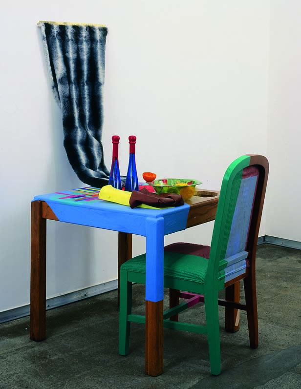 2003 wooden table, two blue glass bottles, flipper, painted shower curtain, acrylic paint, pink upholstered chair, fur on hinge, plastic bowl, plastic orange 58.5 x 53 x 30 in 148.6 x 134.6 x 76.2 cm